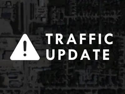 Caution symbol and text reads, "Traffic Update," on a blurred darkened aerial photo of Steinbach.